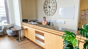 A reception area with a wooden counter, a clock, and a whiteboard. - Opul Boutique (Douglas)