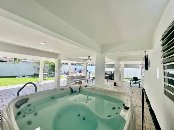 A covered outdoor area with a hot tub, patio furniture, and a view of the backyard.