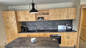 Eine Küche mit Holzausstattung, einer Granitarbeitsplatte, einem Spülbecken, einer Kaffeemaschine, einer Mikrowelle und drei Barhocker.