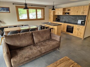 A modern kitchen with wooden cabinets, a central island, and a dining area with a brown sofa and chairs.
