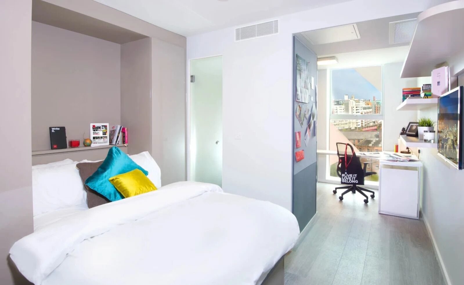 A modern hotel room with a bed, a desk, and a view of the city.