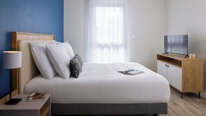 Een moderne hotelkamer met een groot bed, een televisie, een nachtkastje en een raam met gordijnen.