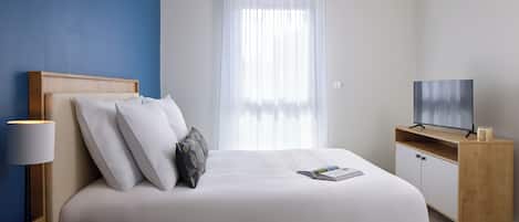 Una habitación de hotel moderna con una cama grande, un televisor, una mesita de noche y una ventana con cortinas.
