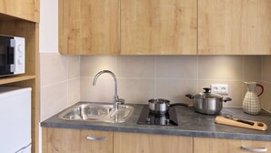 Een keuken met houten kastjes, een roestvrijstalen spoelbak, een magnetron, een pan op een inductiekookplaat en een vaas.