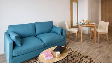 Una sala de estar moderna con un sofá azul, una mesita redonda con una computadora portátil, un libro y una vela.
