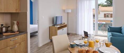 A modern hotel room with a dining area, kitchenette, and a balcony with a view.