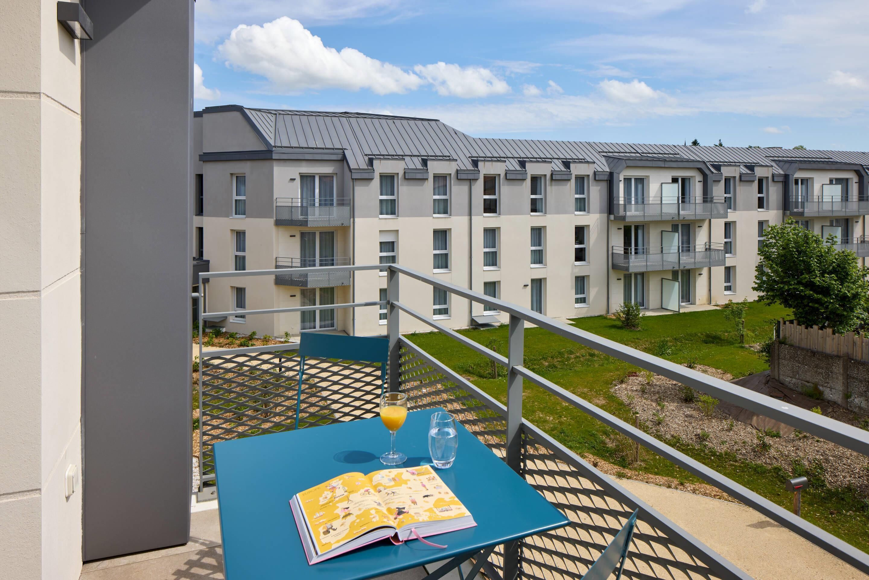 A balcony with a table, a book, and a glass of orange juice.