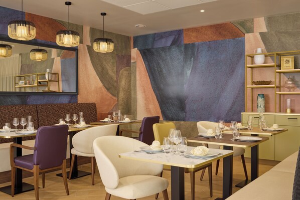 Un interior de restaurante moderno con arte mural geométrico, iluminación colgante y mesas y sillas ordenadas.