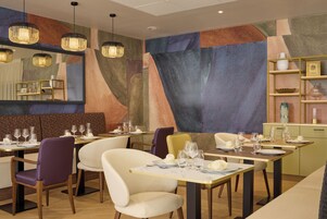 Un intérieur de restaurant moderne, agrémenté d’œuvres d’art géométriques sur les murs, de luminaires suspendus et de tables et de chaises disposées avec soin.