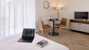 Een hotelkamer met een bed, een laptop, een televisie, een tafeltje met stoelen en een lamp.