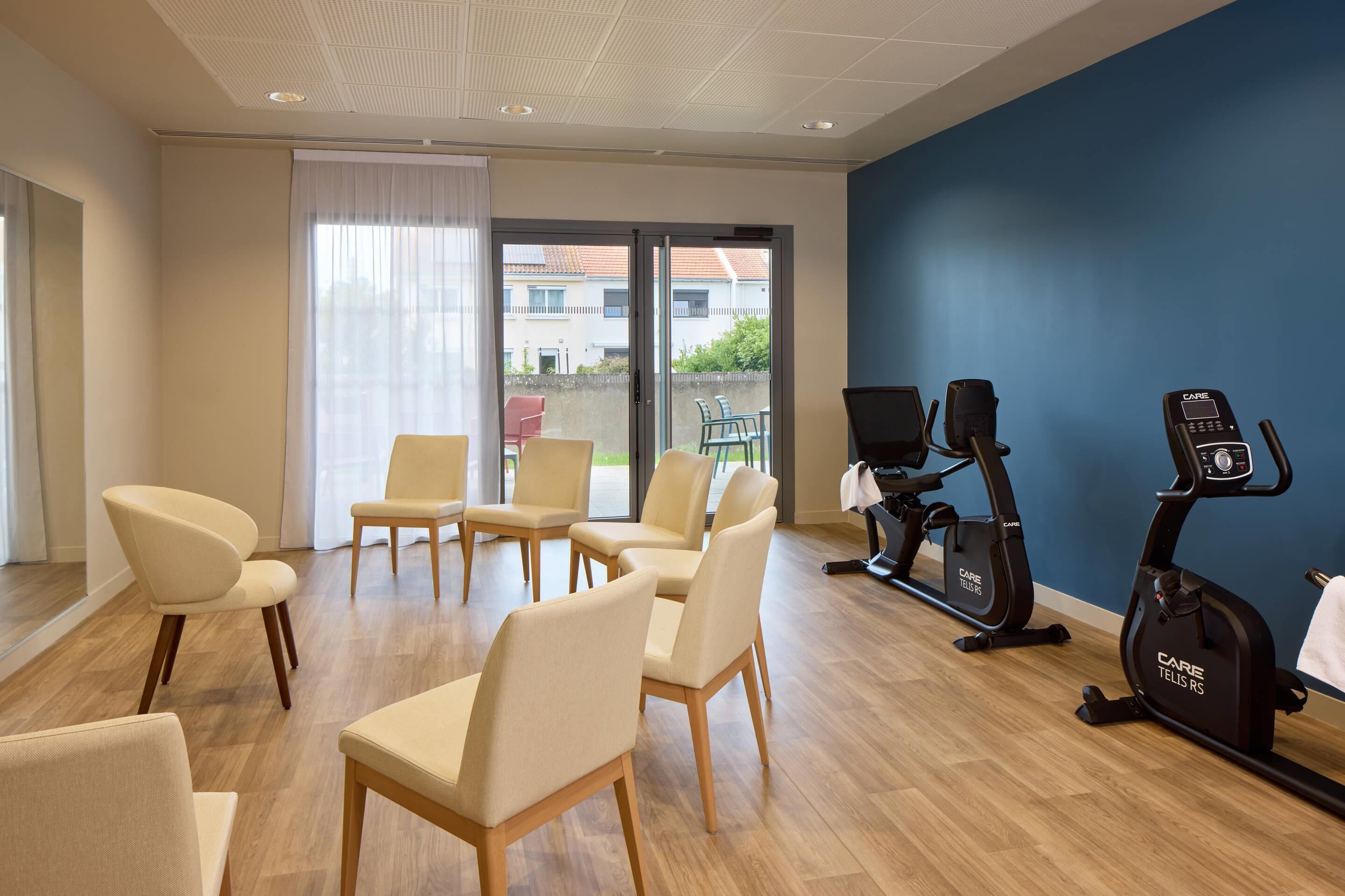 Una habitación con equipo de ejercicio, incluyendo una bicicleta estática y una cinta de correr, además de varias sillas.