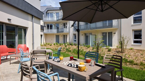Een terras buiten met een eettafel, omringd door stoelen, en een parasol voor de schaduw.