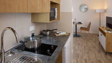 Une cuisine compacte équipée d’un évier, d’une cuisinière et d’un four à micro-ondes. On y trouve une chaise et une petite table avec une lampe.