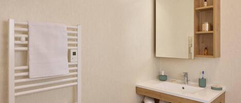 A modern bathroom with a white towel rack, a wooden vanity with a mirror, and a shelf with toiletries.