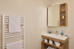 Un baño con toallero blanco, tocador de madera con espejo y repisa con artículos de aseo.