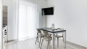 A modern dining area with a table, chairs, a flat-screen TV, and a kitchen area with cabinets. - Three-room apartment Scola 11 (Gabicce Mare)