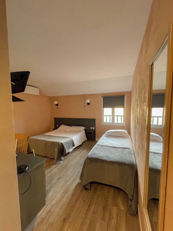 Quarto de hotel compacto com duas camas de solteiro, uma escrivaninha com cadeira, uma mesinha e um espelho.