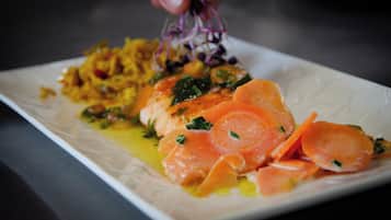 A plate of food with salmon, carrots, and a hand sprinkling seasoning.