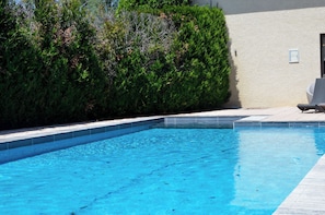 A swimming pool with a tiled edge, surrounded by a hedge and a building with a light-colored wall. - Maison Legate (Saint-Beauzire)