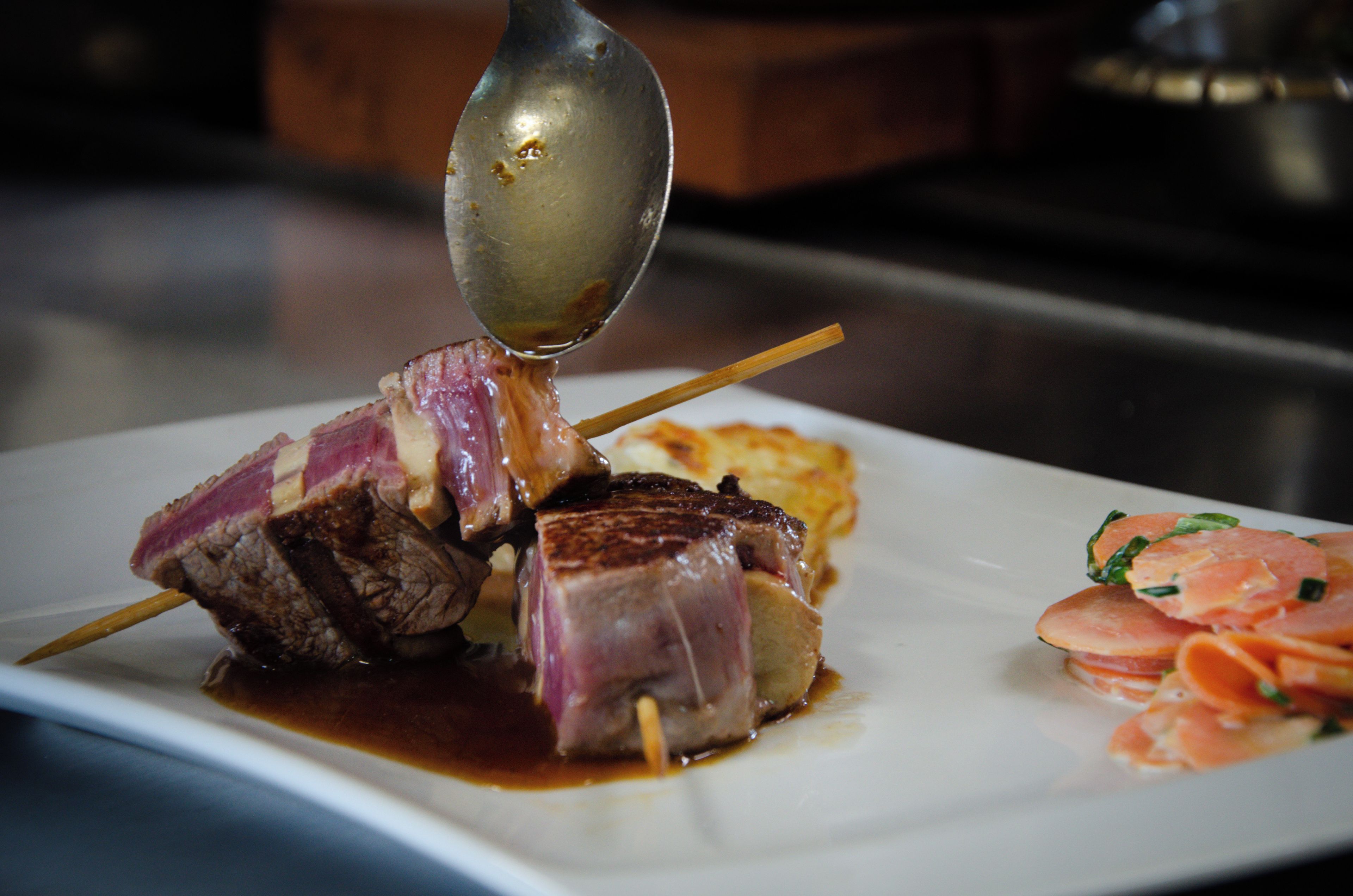 A plate with skewered meat, a spoon, and some vegetables.
