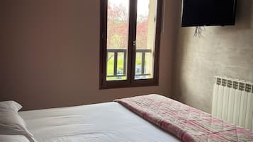 A bedroom with a bed, a window, a radiator, and a TV mounted on the wall.
