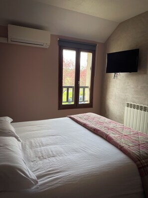 A bedroom with a bed, a window, a radiator, and a TV mounted on the wall. - Maison Legate (Saint-Beauzire)