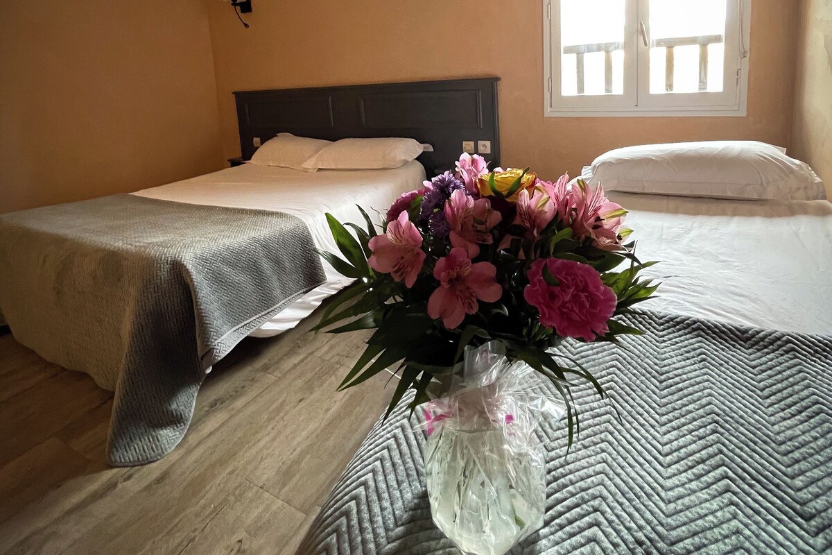 A hotel room with two beds, a window with a view, and a vase with flowers on the bed.
