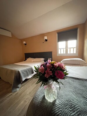 A hotel room with two beds, a window with a view, and a vase with flowers on the bed. - Maison Legate (Saint-Beauzire)