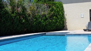 Μια πισίνα με πλακάκια στην άκρη, περιτριγυρισμένη από έναν φράχτη και ένα κτίριο με έναν τοίχο σε ανοιχτόχρωμο χρώμα.