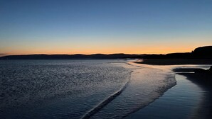 Ein Strand mit ruhiger See und sanften Hügeln im Hintergrund.