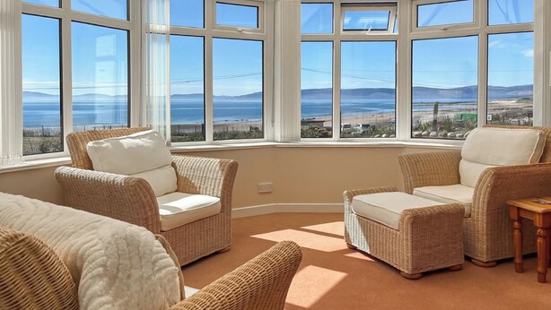 Ein Zimmer mit Korbmöbeln, großen Fenstern und Meerblick.