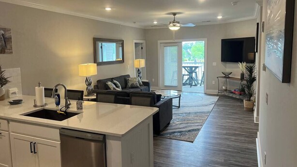 A modern kitchen with a central island, a dining area with a sofa, and a large window overlooking a deck. - Luxury Condo at Crow Creek golf resort (Brunswick County)