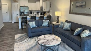 A modern living room with a grey sofa, a round coffee table, and a dining area in the background. - Luxury Condo at Crow Creek golf resort (Brunswick County)