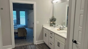 A bedroom with a bed, a bathroom with a sink and mirror, and a hallway with a door. - Luxury Condo at Crow Creek golf resort (Brunswick County)