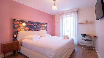 Un dormitorio con una cama grande, una mesita de noche, un escritorio con una silla, un televisor y una ventana con cortinas.