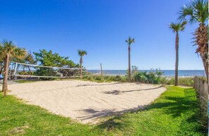 A beach volleyball court with a net, surrounded by sand, grass, and palm trees. - Awesome Modern Direct Oceanfront Paradise (Myrtle Beach)