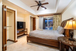 A bedroom with a bed, a television, a ceiling fan, and a window with curtains.