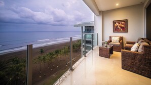 A balcony with a view of the beach and ocean, wicker furniture, and a painting on the wall.