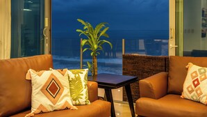 A room with a view of the ocean, a brown leather sofa, a small table, and a potted plant.