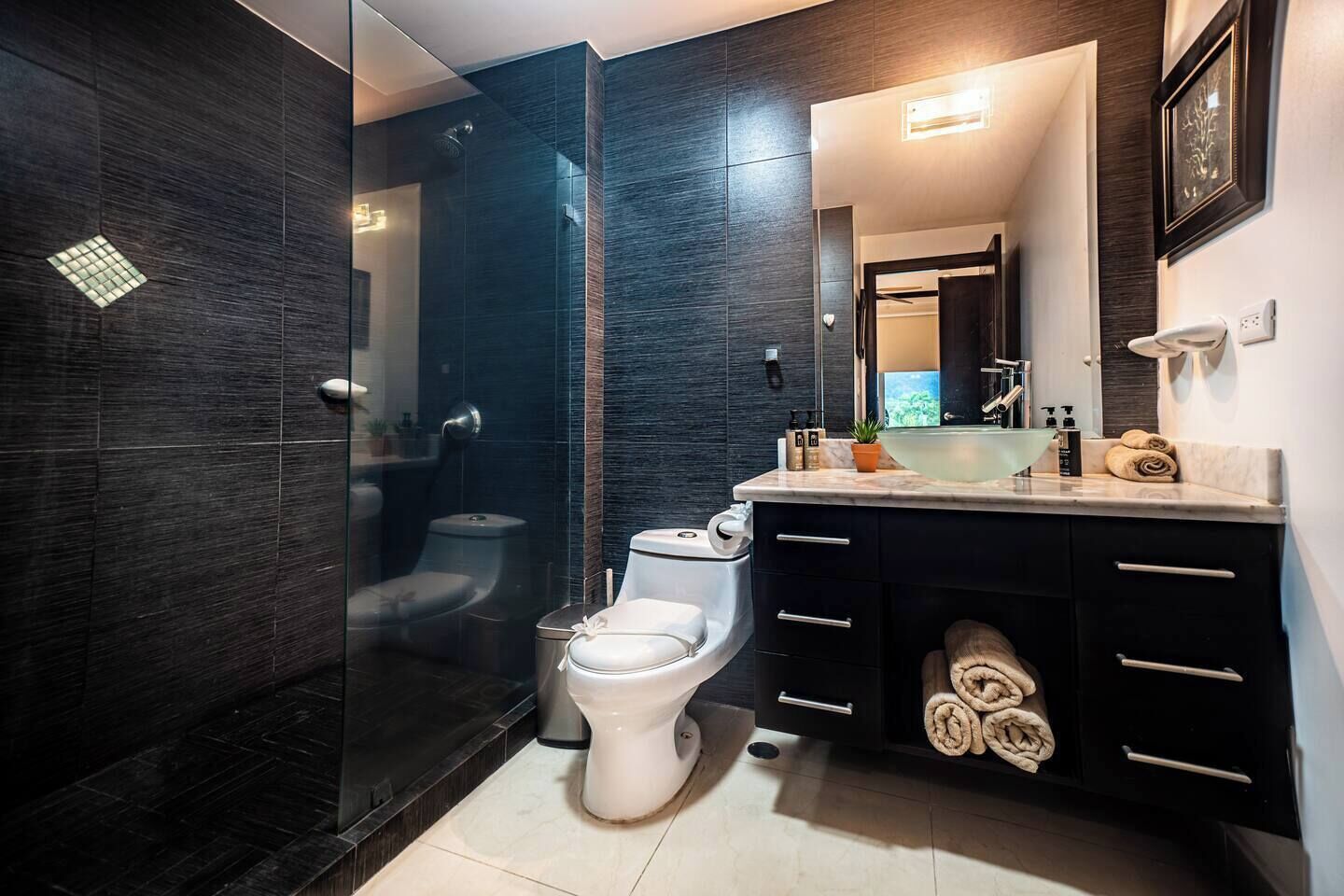 Een moderne badkamer met een douchecabine van glas, een wit toilet en een wastafel met spiegel en handdoekhouder.