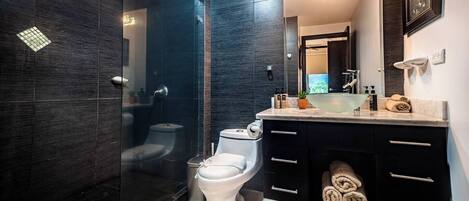 Een moderne badkamer met een douchecabine van glas, een wit toilet en een wastafel met spiegel en handdoekhouder.