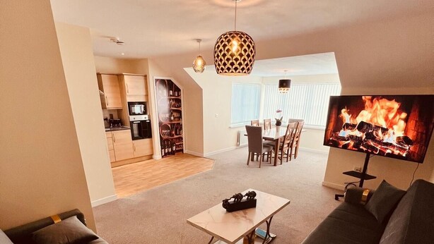 A modern living room with a sofa set, a coffee table, and a flat-screen TV displaying a fireplace. - Relaxing Enjoyable Stay IN middlesbrough TS5 (Middlesbrough)