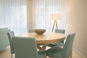 Une table de salle à manger ronde, surmontée d’un saladier, entourée de six chaises, dans une pièce dotée de rideaux légers et d’un lampadaire.