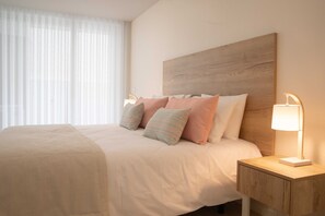 Un lit bien fait, avec une tête de lit en bois, une table de chevet avec une lampe et des rideaux légers.