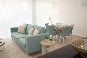 A living room with a sofa, a dining table with chairs, a lamp, and a small table with a bowl.