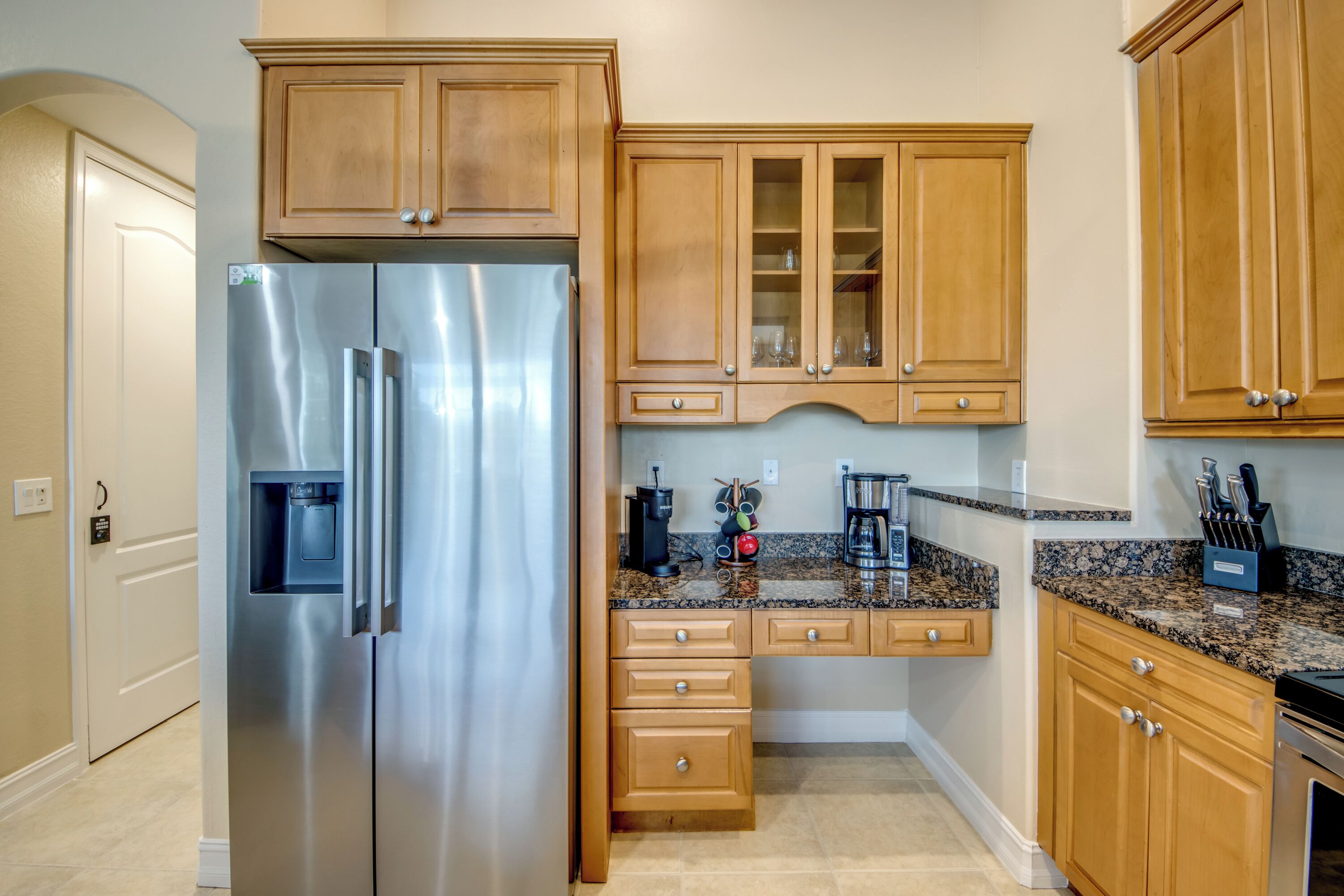 Una cocina con armarios de madera, refrigerador de acero inoxidable, encimeras de granito y una cafetera.
