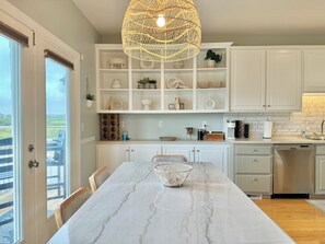 A modern kitchen with white cabinetry, a marble countertop, and a hanging wicker light fixture. - The Vida Sol! Steps to the Ocean. Sound views, Sunsets, Pier + Kayak launch (North Topsail Beach)