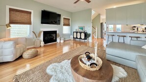 Un salón amplio con chimenea, ventilador de techo y una cocina visible a través de un arco.