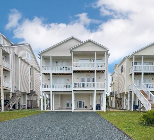A multi-story hotel with balconies, a central entrance, and a gravel driveway. - The Vida Sol! Steps to the Ocean. Sound views, Sunsets, Pier + Kayak launch (North Topsail Beach)