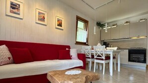 Ein modernes Wohnzimmer mit einem roten Sofa, einem kleinen Holztisch und einem Essbereich mit weißen Stühlen.